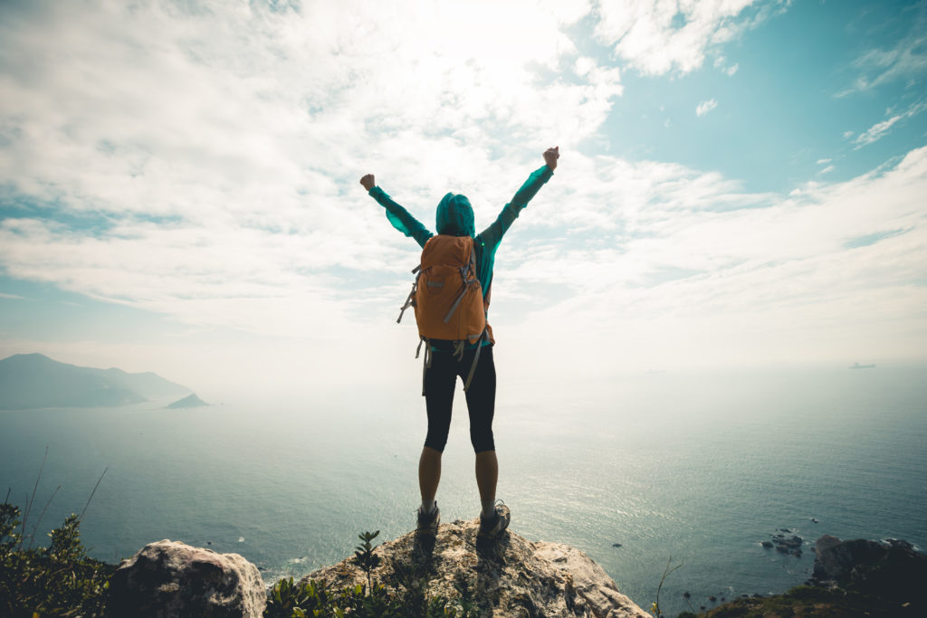 Successful hiker outstretched arms at seaside mountain top cliff edge